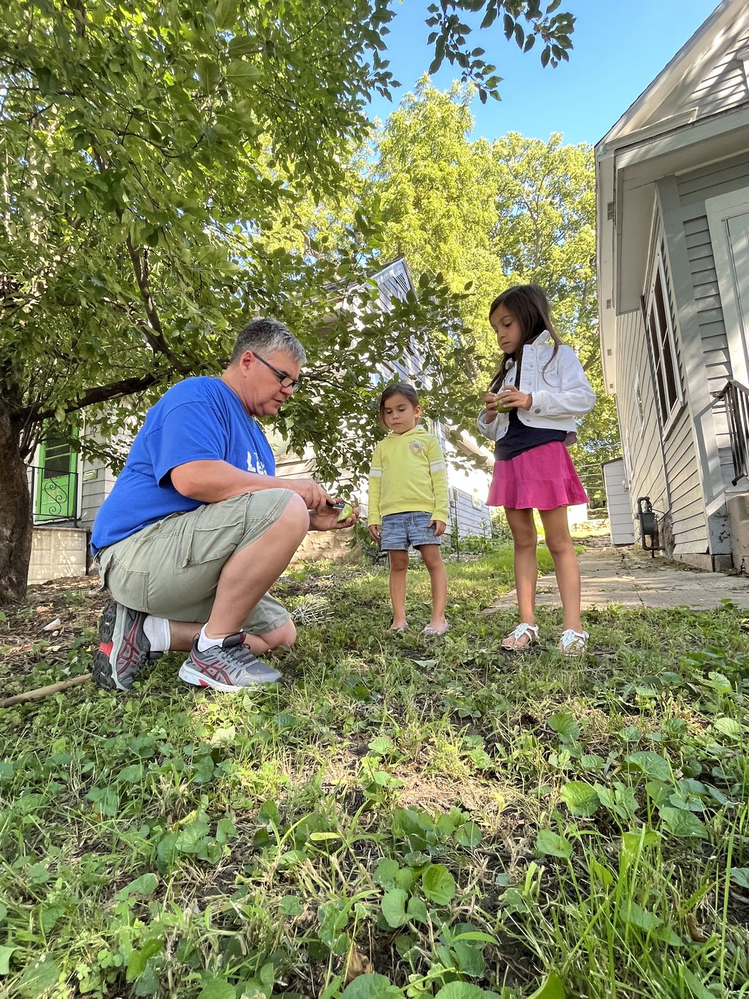 Toby Leonard crouching in a yard with two children looking at apples they have gathered