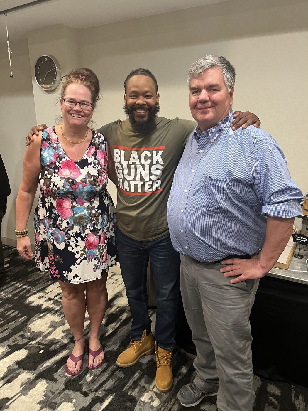 Toby Leonard with two community members, arms around each other, at an indoor gathering